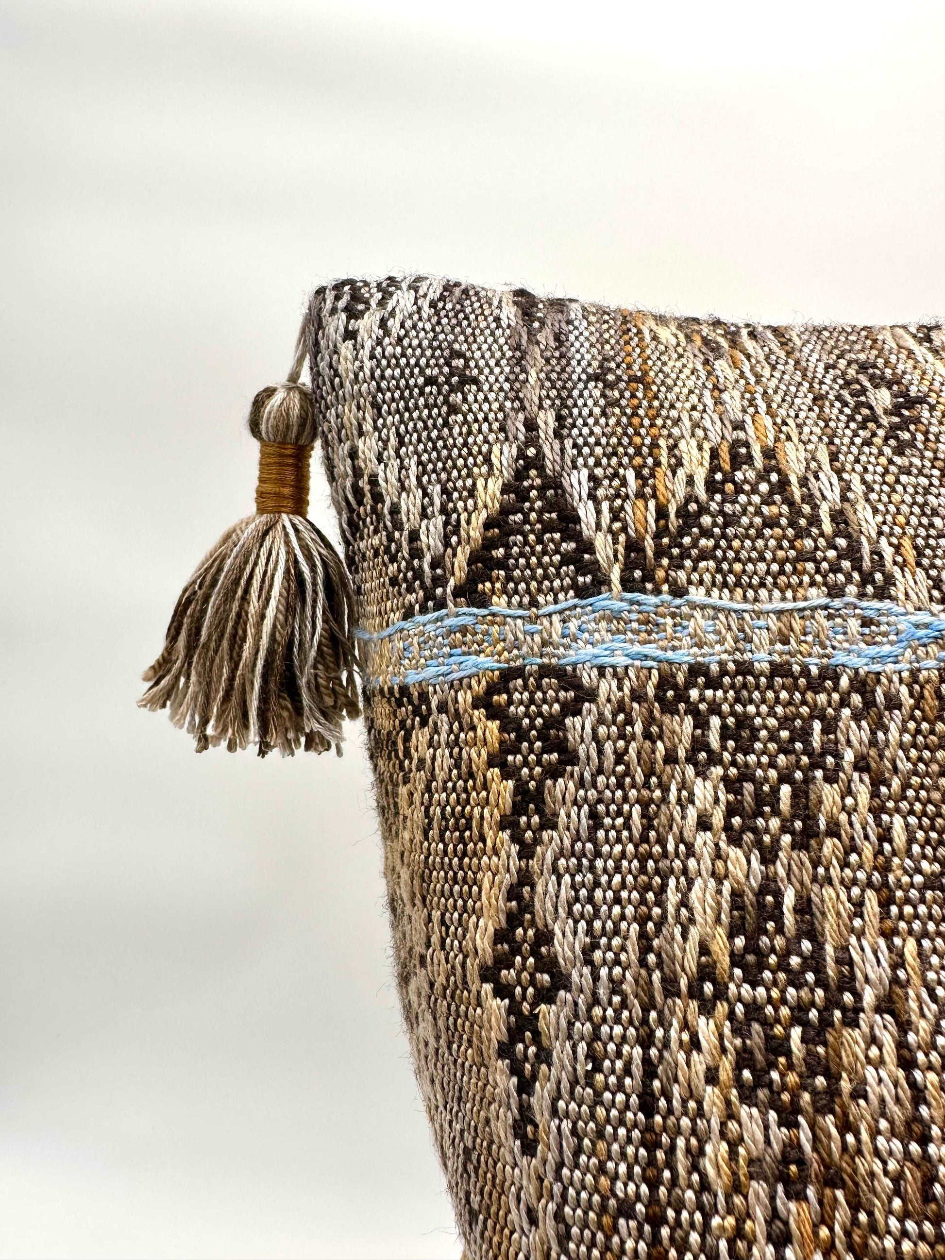 Neutral Brown toned handwoven pillow cover with light blue details and tassels in the corners