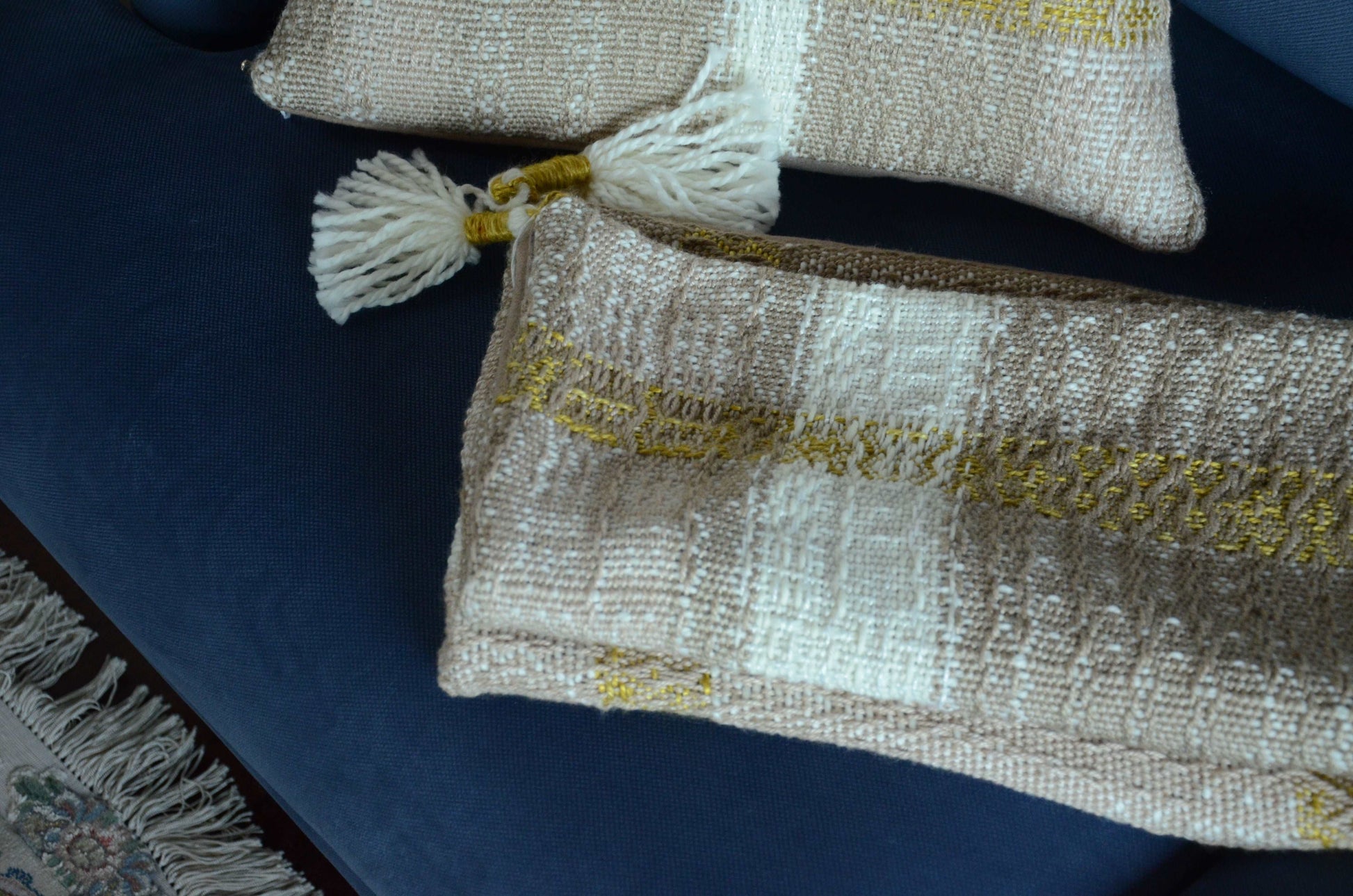 Neutral cream colored throw pillow cover on couch with tassels and golden yellow weaving detail