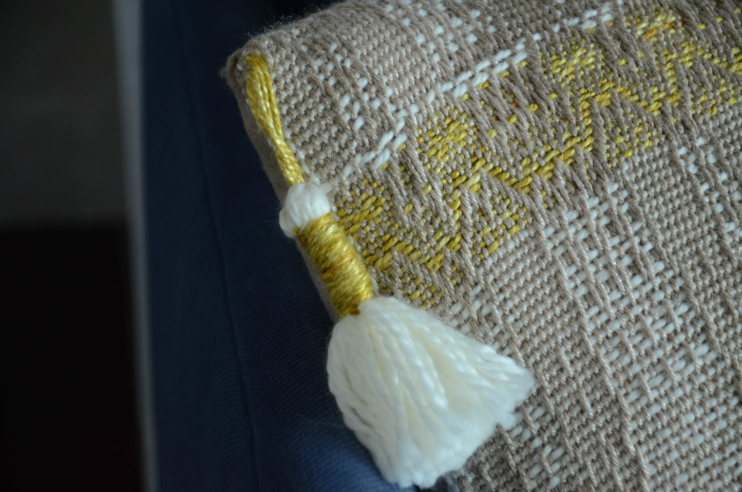 Neutral cream colored throw pillow cover on couch with tassels and golden yellow weaving detail