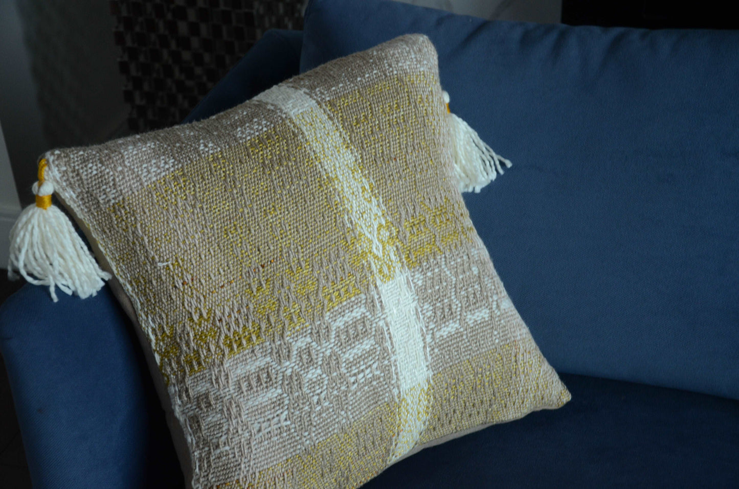 Neutral cream colored throw pillow cover on couch with tassels and golden yellow weaving detail