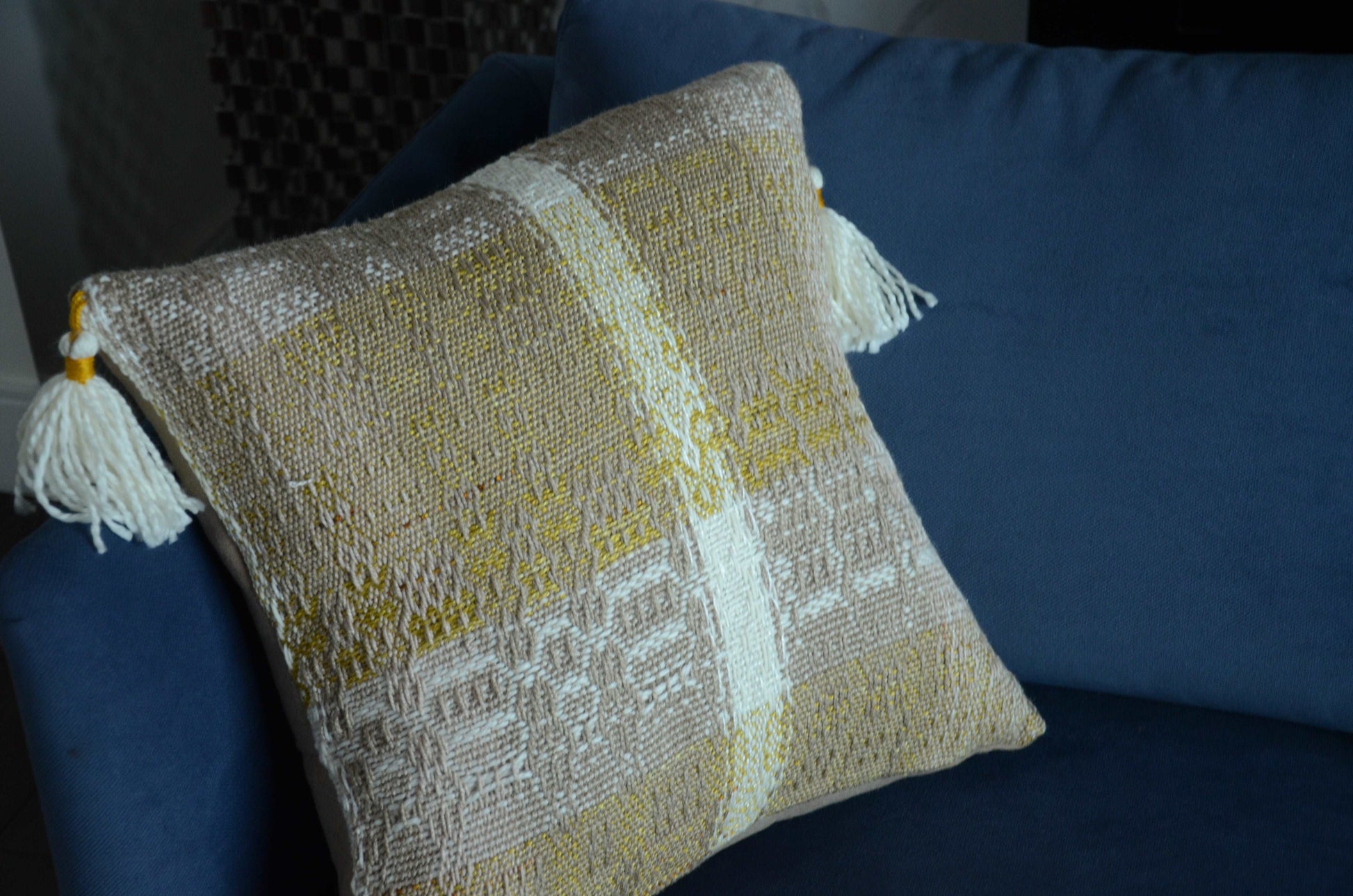 Neutral cream colored throw pillow cover on couch with tassels and golden yellow weaving detail