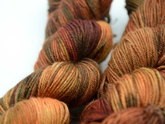 warm toned orange hand painted and hand dyed knitting yarn with dark army green notes