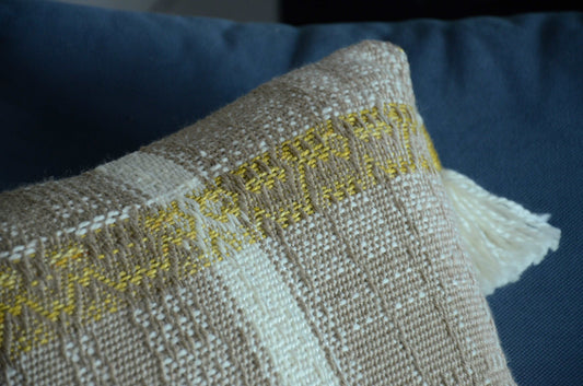 Neutral cream colored throw pillow cover on couch with tassels and golden yellow weaving detail